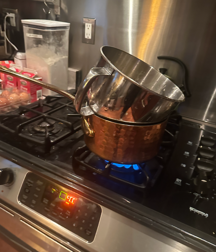 The bowl of a stand mixer resting over a pot of simmering water.